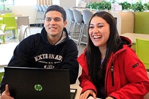 Dos jóvenes sonriendo frente a un computador portátil